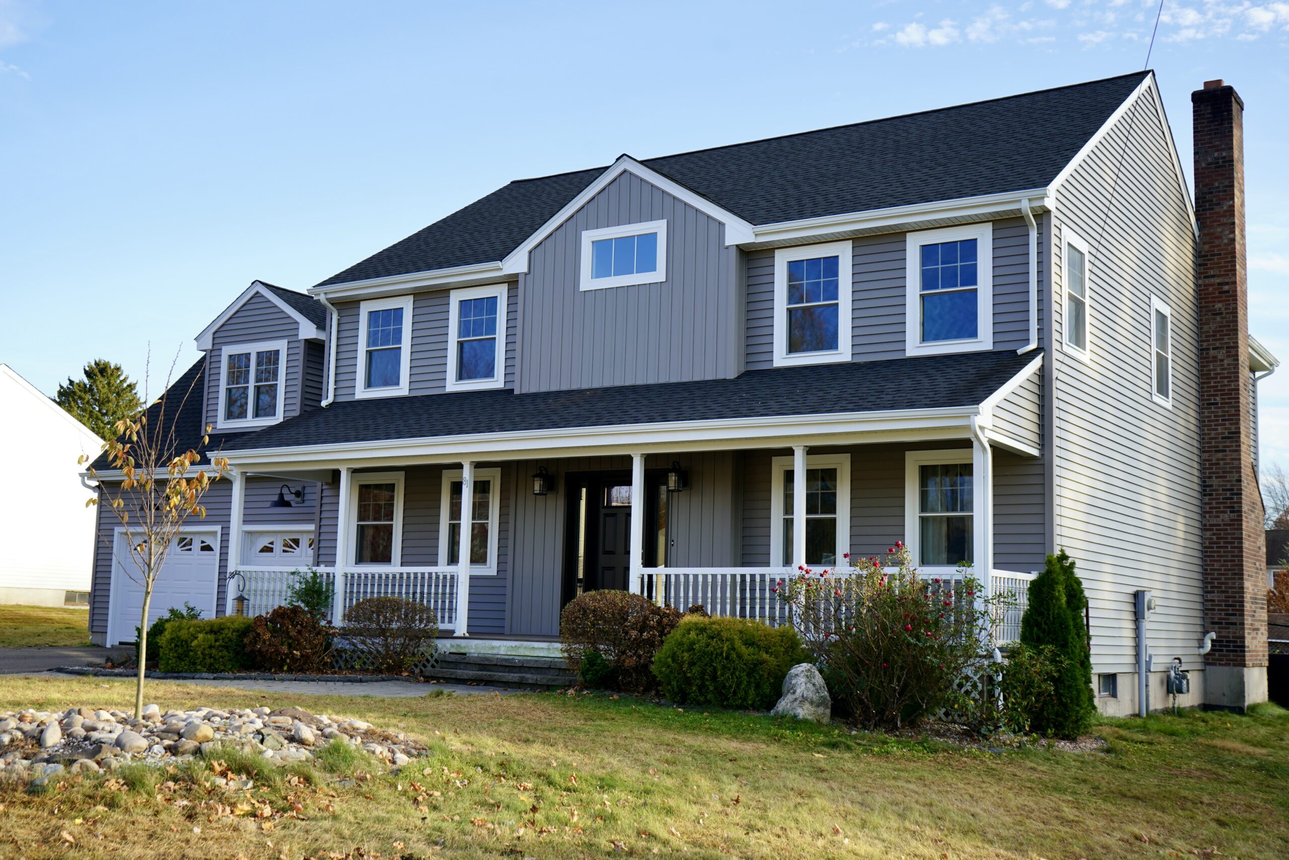 Newly updated home exterior featuring fresh vinyl siding in a modern gray finish, complemented by a clean and inviting front porch and well-maintained landscaping.